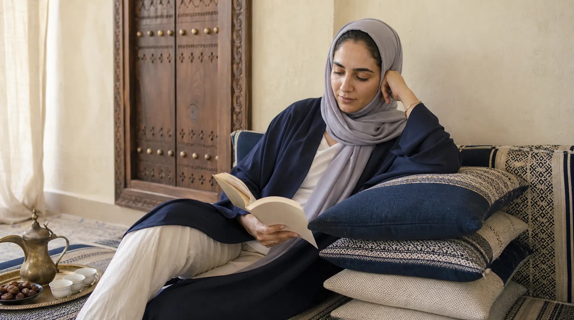 امرأة عُمانية تستريح مسنودة إلى وسائد مكدّسة في المنزل وهي تقرأ.