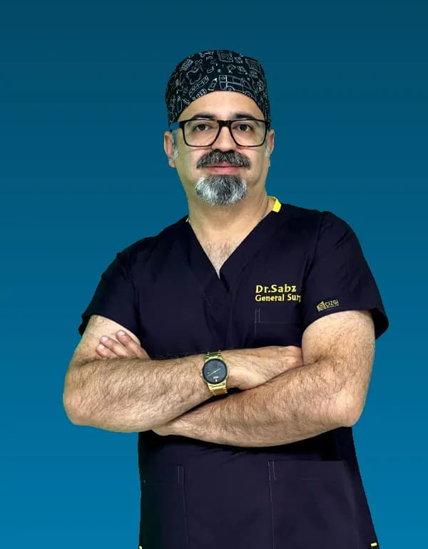 صورة للدكتور سيد علي سبز بزي جراحي كحلي وقبعة جراحية مزخرفة، واضعا ذراعيه متقاطعتين أمام خلفية بسيطة.